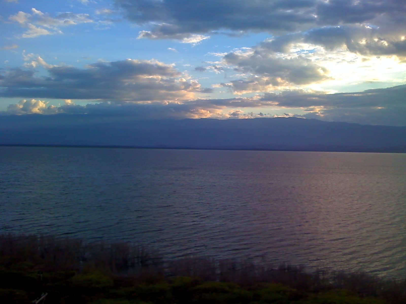 Vista del Lago Enriquillo con el agua en primer plano y la sierra al fondo bajo un cielo despejado