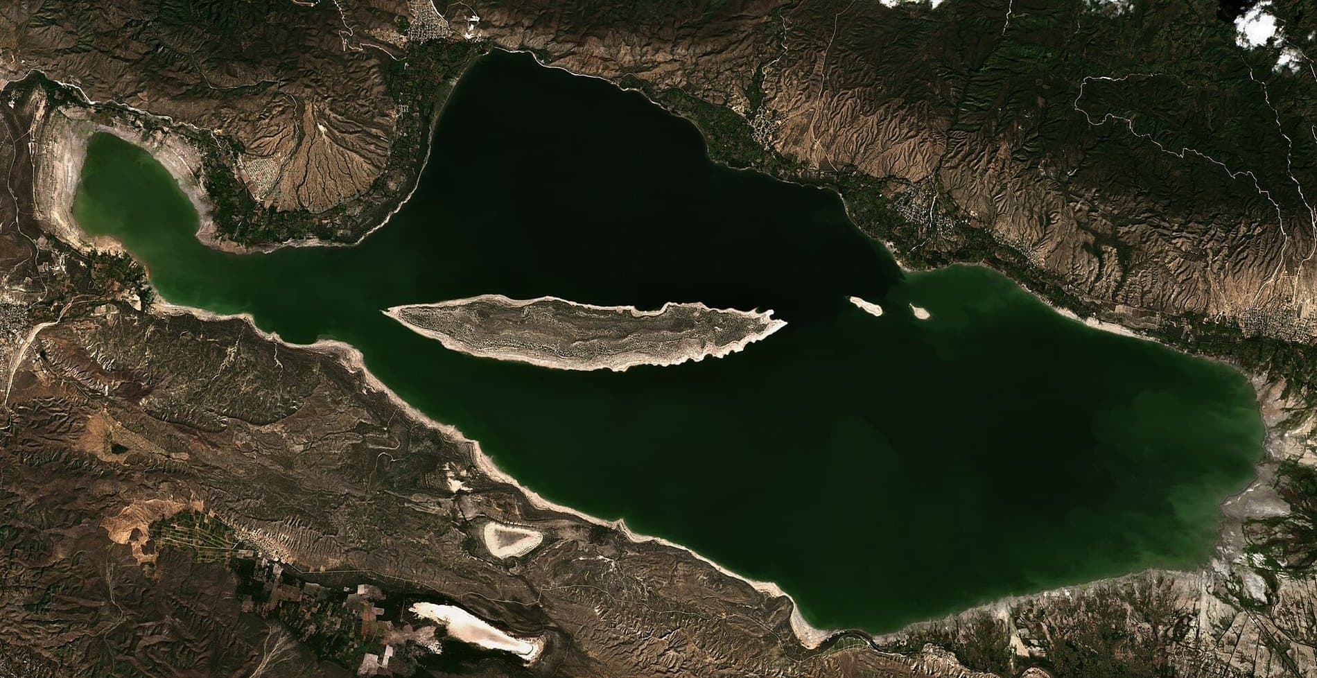 Imagen de satélite del Lago Enriquillo: una mancha oscura alargada encajada entre dos cordilleras, con la Isla Cabritos en el centro